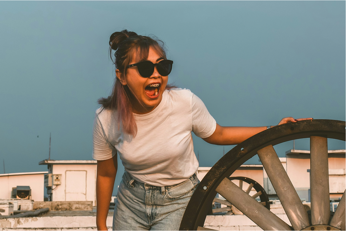 Person wearing sunglasses and a white t-shirt on a rooftop with a clear sky.